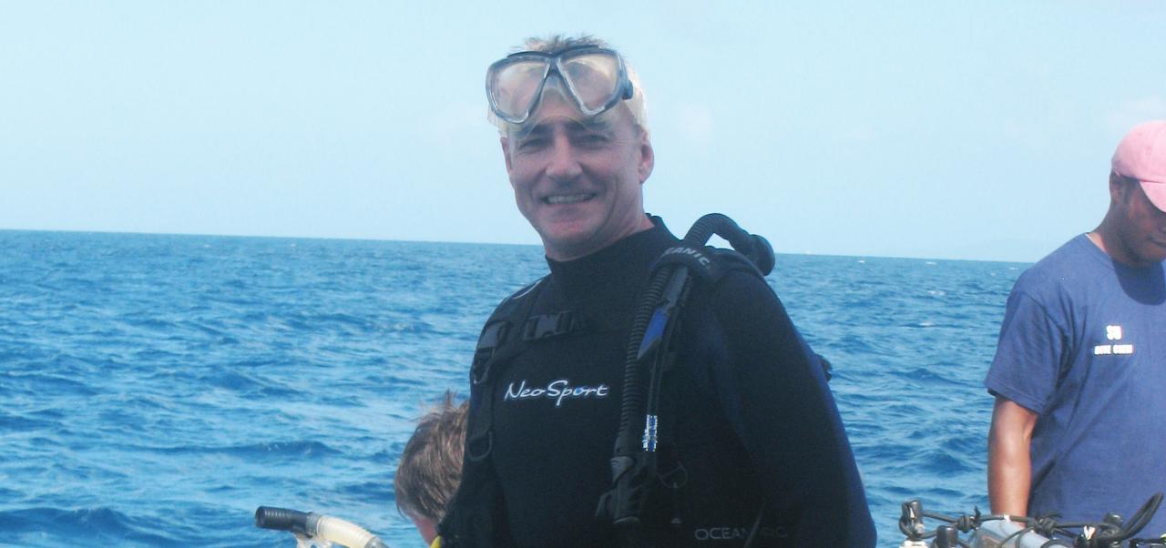 On a boat in the ocean, Paul Meadows smiles while wearing a scuba diving outfit