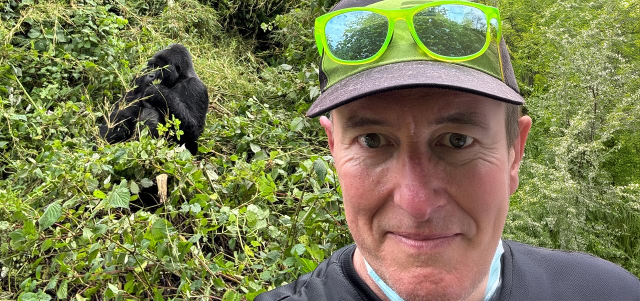 On a snowy mountaintop in Colorado, Scott Robinson wears green sunglasses and a helmet while taking a selfie with his red mountain bike behind him