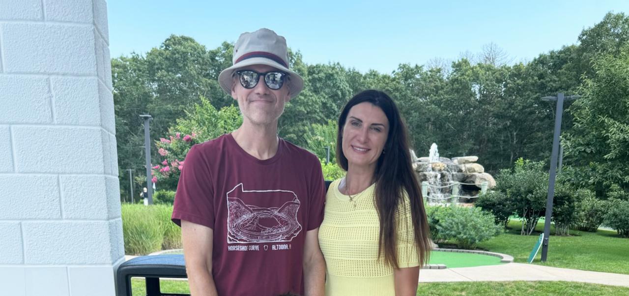 Dr. Steven Goss,  Clinical faculty member and chair of the Management and Technology program in the Division of Programs in Business at NYU SPS, poses for a photo with his wife on a putting green.
