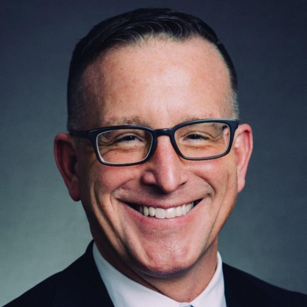 Headshot of Timothy Savage smiling in glasses and a suit