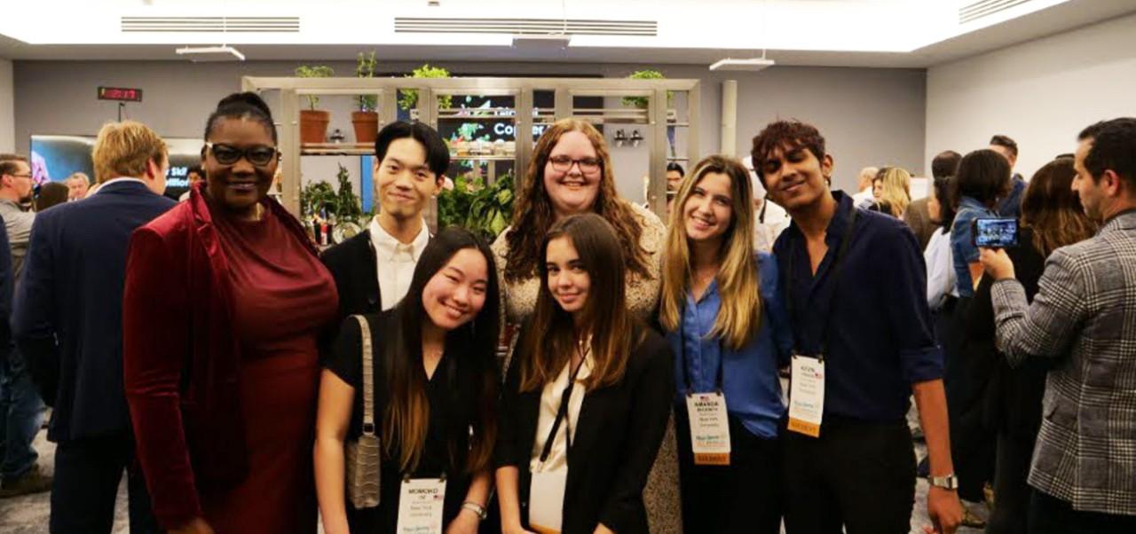 Payten Slack, student at the Jonathan M. Tisch Center of Hospitality, NYU SPS, poses for ap hoto with a group of friends at an indoor event.