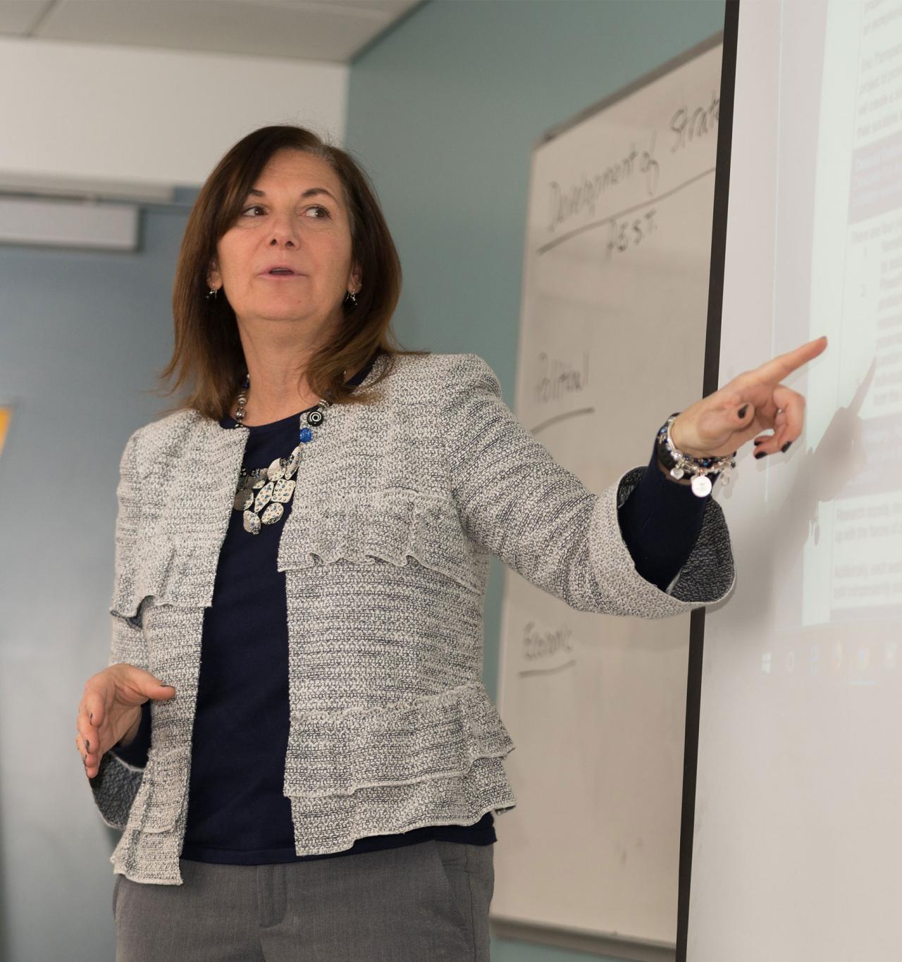 Woman speaking and pointing to projector screen