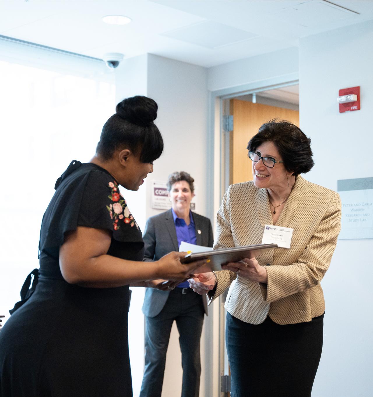Smiling woman presenting an award to a woman in a black dress