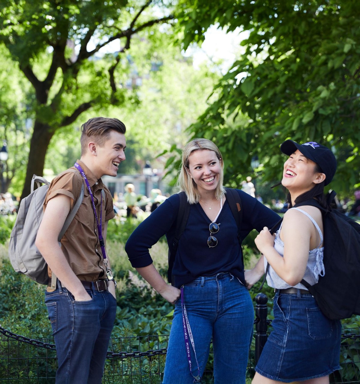 Two people smile and chat in a park with autumn foliage, standing near lush greenery.