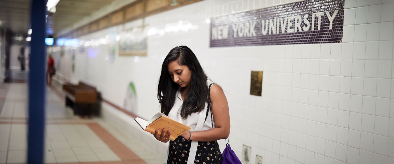 Student waiting at New York University Subway stop reading a book.