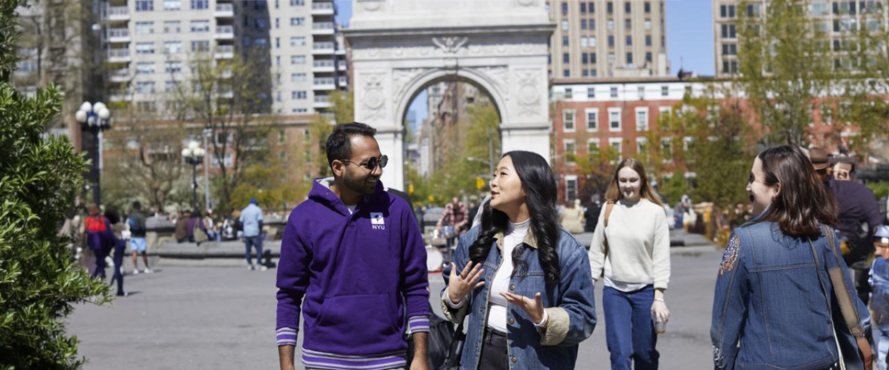 Three NYU SPS students are slightly blurry as they run across a busy NYC crosswalk and two of them are wearing NYU t-shirts